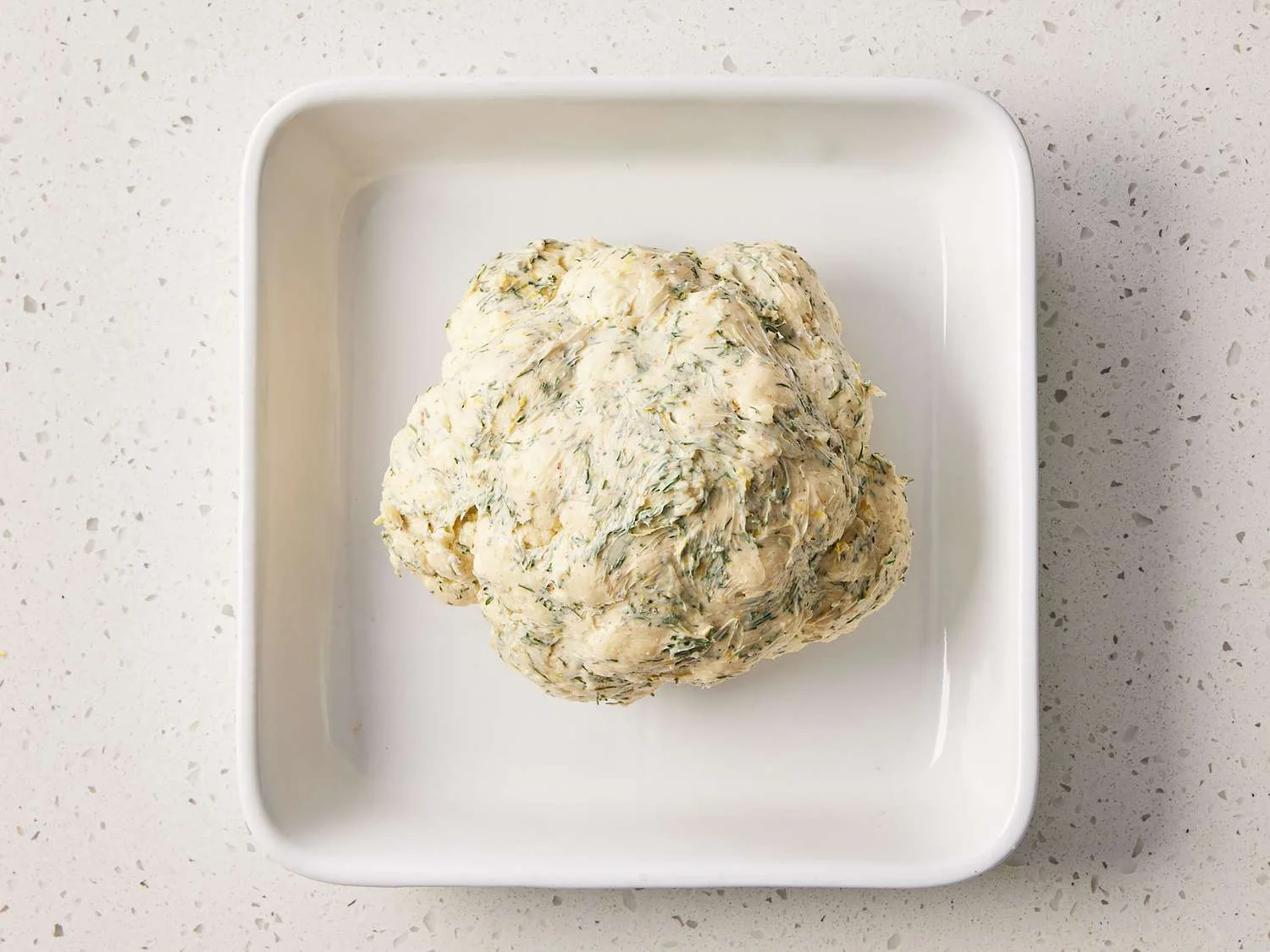 Spread butter mixture evenly over the top and sides of cauliflower, place in a casserole dish, and cover with foil.