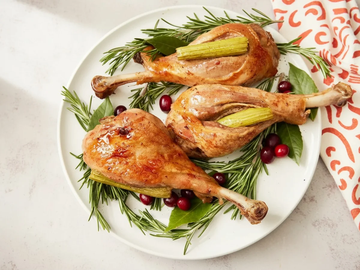 Overhead looking down at a few roasted turkey legs served on a platter with rosemary and cranberry garnishes.