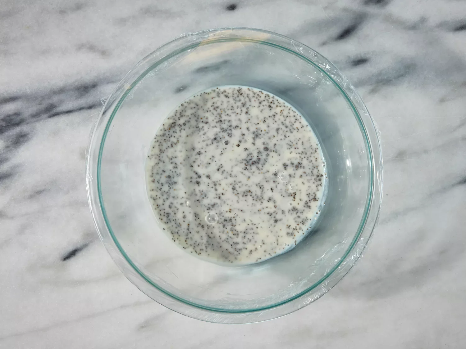 Chia pudding mixture soaking in a glass bowl covered with plastic wrap.